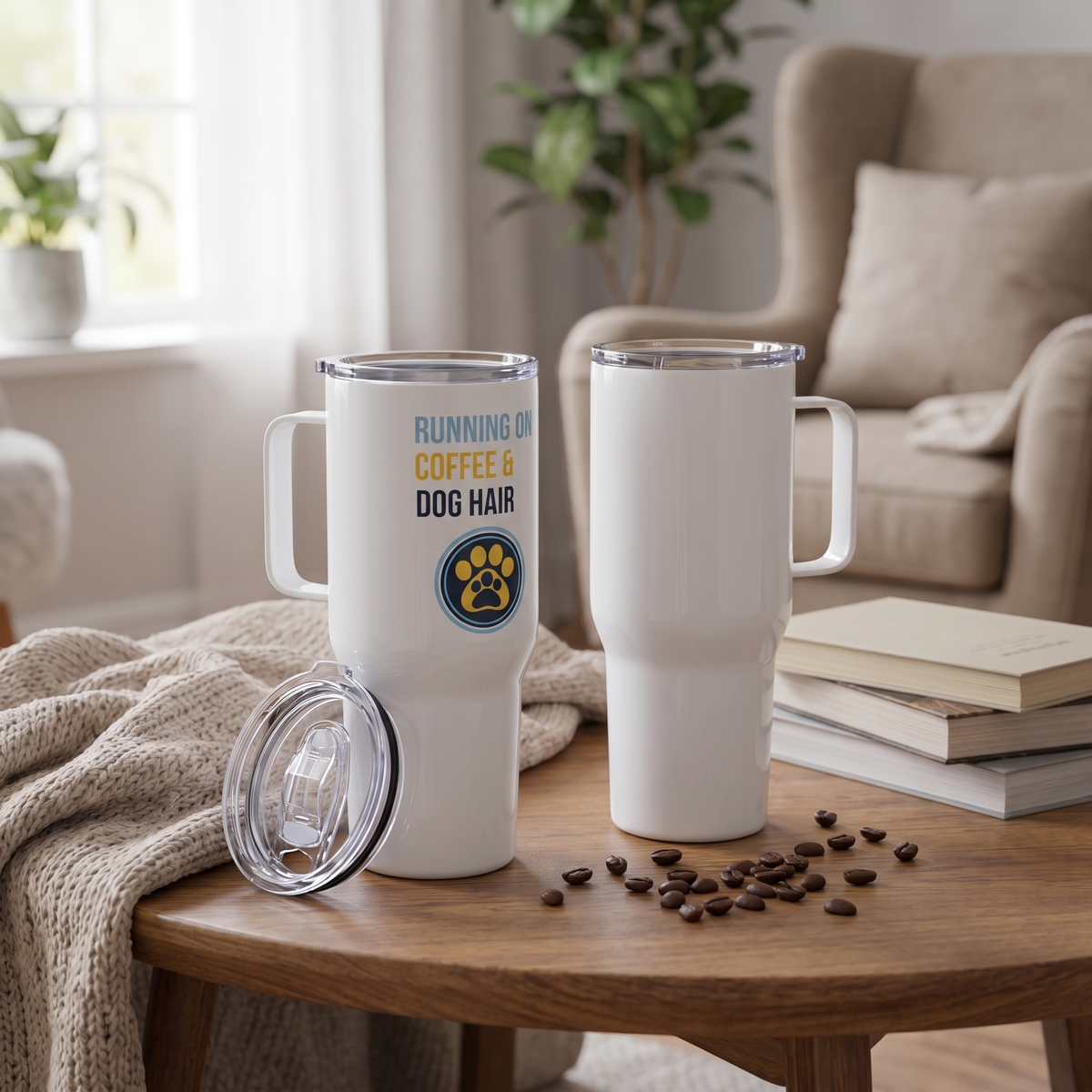 Two white insulated travel mugs with clear lids are shown on a wooden table in a cozy living room setting. One mug is upright with a printed slogan reading 'RUNNING ON COFFEE & DOG HAIR' and a paw print logo, while the other is empty.